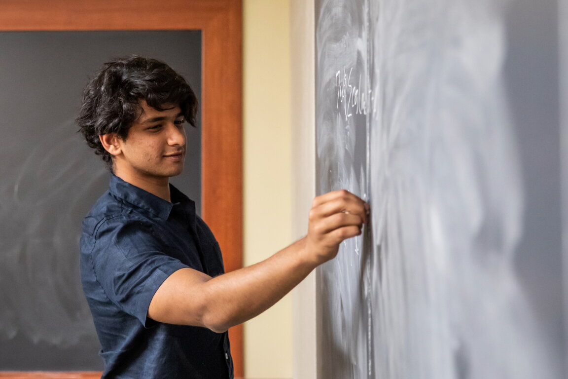 A student works on a math problem on a chalkboard.